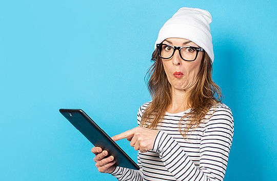 Eine Frau deutet mit skeptischer Miene auf ein Tablet.