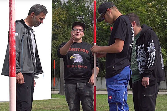 Drei junge Männer und ein Mann mittleren Alters auf Rasen stehen um eine rot-weiße Stange herum