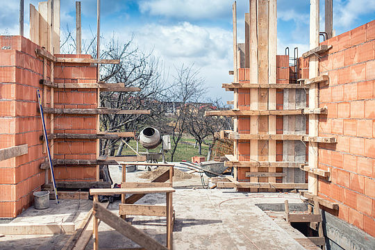 Haus-Baustelle mit roten Ziegelsteinmauern und Betonmischer.