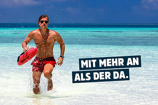 Foto: ein Rettungsschwimmer in Badehose an einem Traumstrand. Text: „Mit mehr an als der da.“