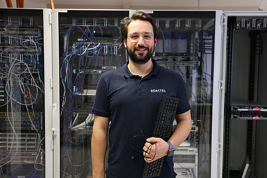 Daniel hält eine Tastatur in der Hand und lächelt in die Kamera.