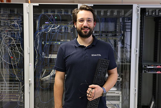 Daniel hält eine Tastatur in der Hand und lächelt in die Kamera.