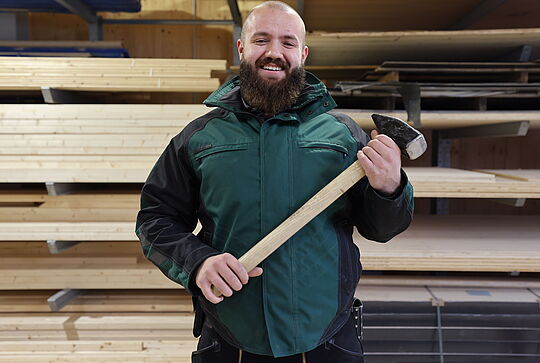 Jonas steht mit einem Hammer vor einem Stapel Holz.