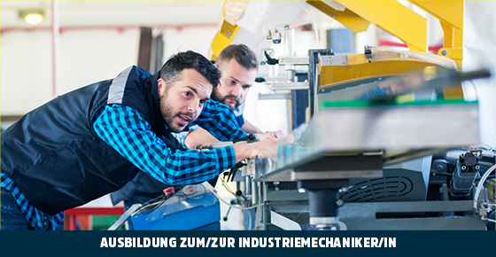 Zwei Männer in blau-karierten Baumwollhemden und blauen Westen stehen gebeugt an einer Maschine und beobachten diese mit analytischem Blick