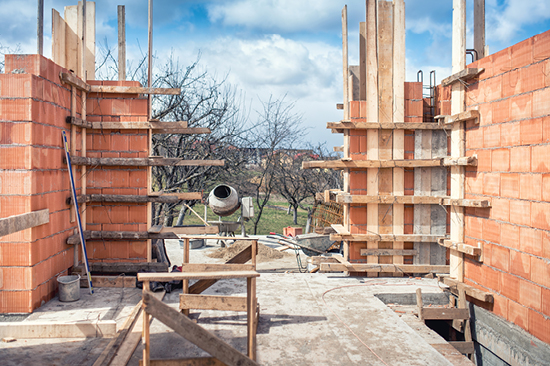 Haus-Baustelle mit roten Ziegelsteinmauern und Betonmischer.