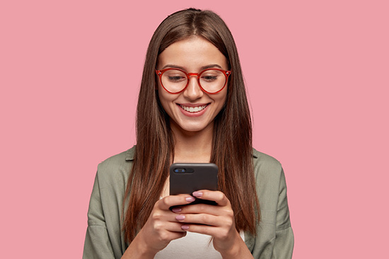Ein Mädchen mit Brille schaut lachend auf ein Handy in ihren Händen. 